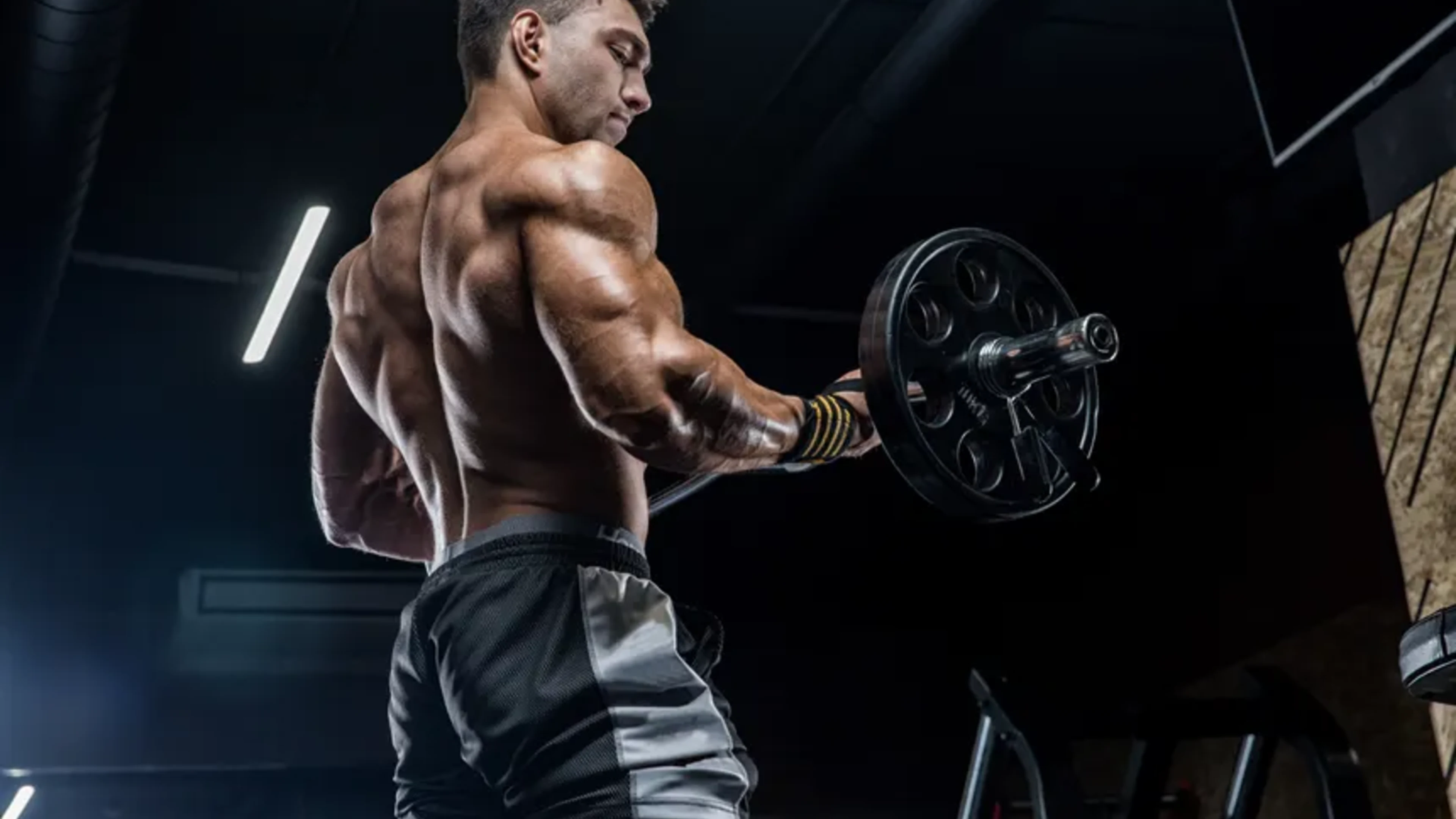 Athlete performing a barbell curl in a dark modern gym