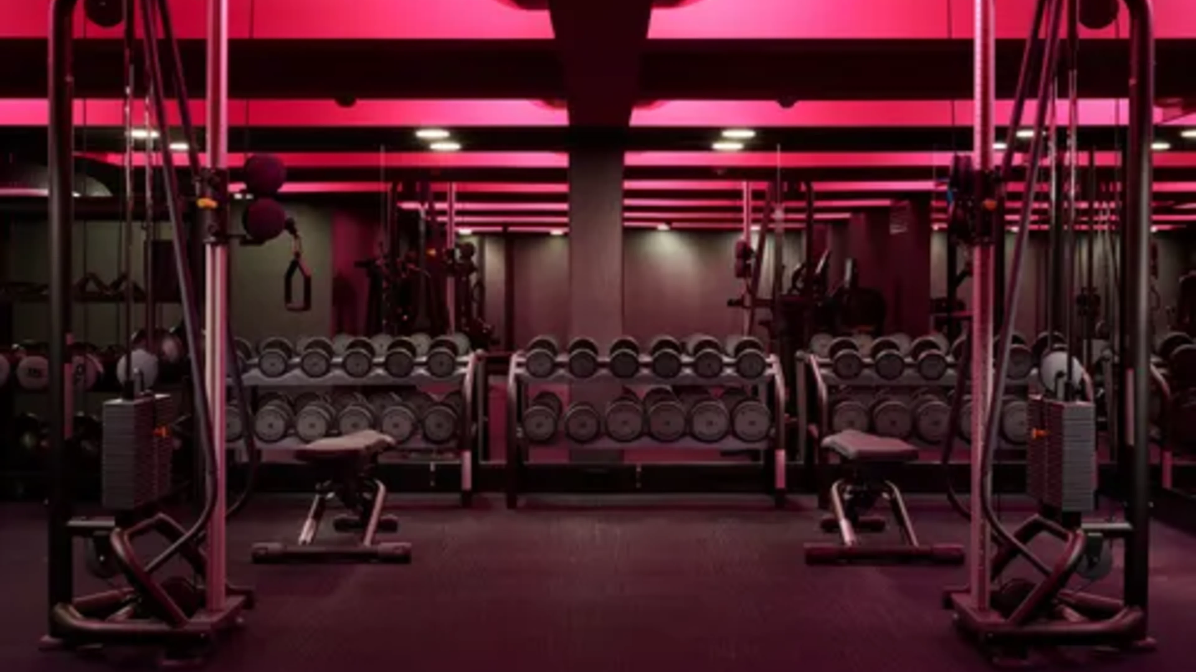 Strength floor with dumbbells and cable machines under red lighting